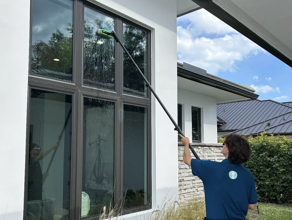 Surf technician cleaning large residential windows with a water-fed pole